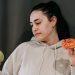 Pensive female wearing casual hoodie deciding between healthy green apple and sweet doughnut in studio