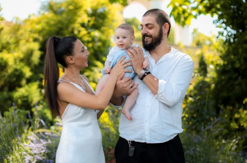 Mother and father joyfully hold their baby in a vibrant outdoor garden setting.