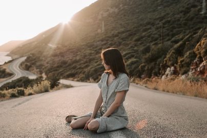 A woman sitting on a coastal road in Antalya during sunset, offering a serene landscape view.